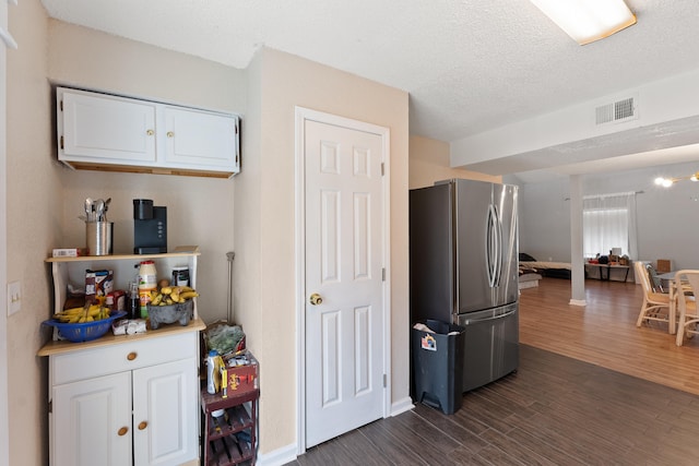 kitchen featuring a textured ceiling, dark wood-type flooring, stainless steel refrigerator, and white cabinetry