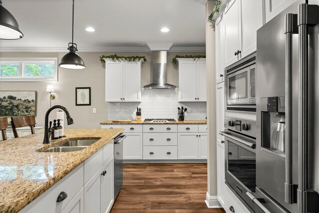 kitchen with appliances with stainless steel finishes, dark wood-type flooring, sink, wall chimney range hood, and white cabinets