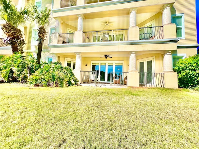 rear view of house featuring ceiling fan, stucco siding, french doors, a yard, and a balcony