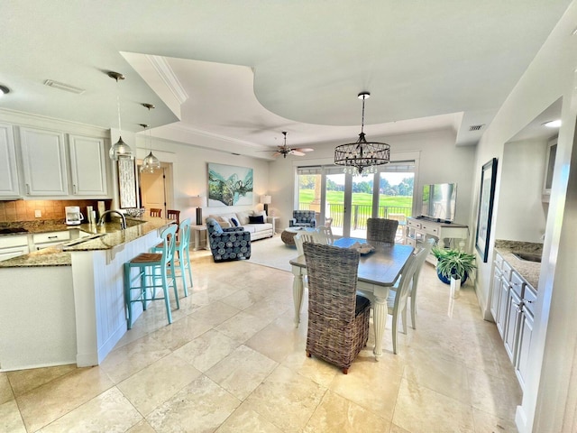 dining area with ceiling fan with notable chandelier, a tray ceiling, crown molding, and sink