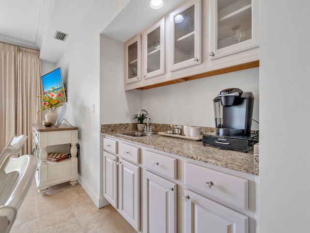 kitchen featuring visible vents, glass insert cabinets, baseboards, light stone counters, and a sink