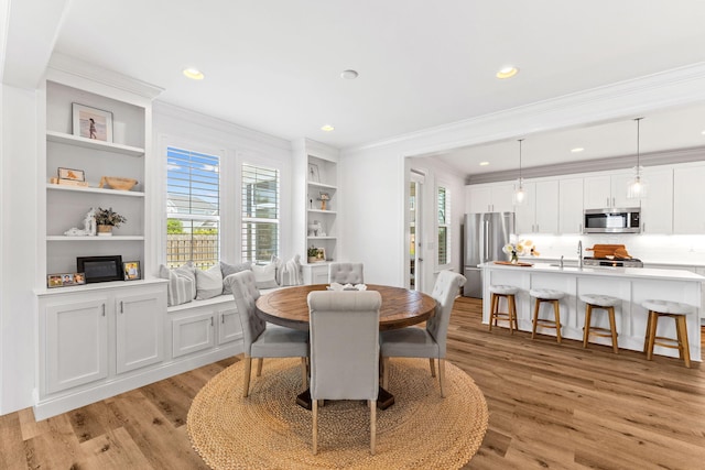 dining space featuring built in shelves, crown molding, and light wood-type flooring