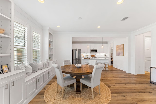 dining space with ornamental molding and light hardwood / wood-style flooring