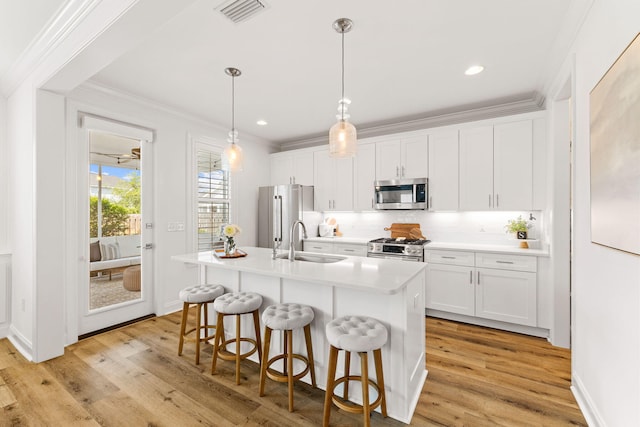 kitchen with a kitchen island with sink, stainless steel appliances, sink, white cabinetry, and light wood-type flooring