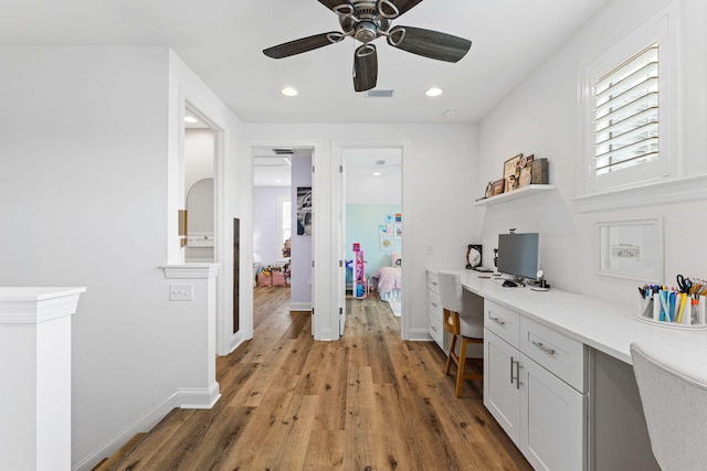 home office with light wood-type flooring, built in desk, and ceiling fan