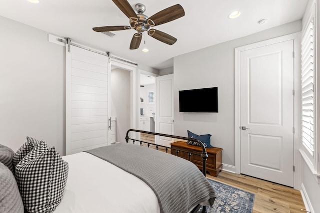 bedroom with a barn door, ceiling fan, and light wood-type flooring