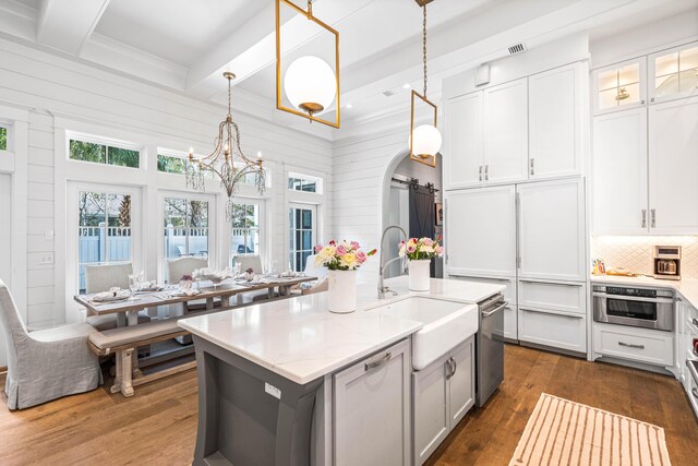 kitchen featuring pendant lighting, an island with sink, beam ceiling, and dark wood-type flooring