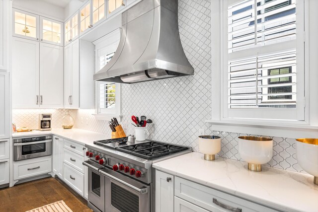 kitchen featuring ventilation hood, white cabinetry, light stone counters, and stainless steel appliances