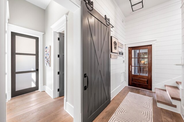 foyer with a barn door, wood walls, a towering ceiling, and hardwood / wood-style flooring