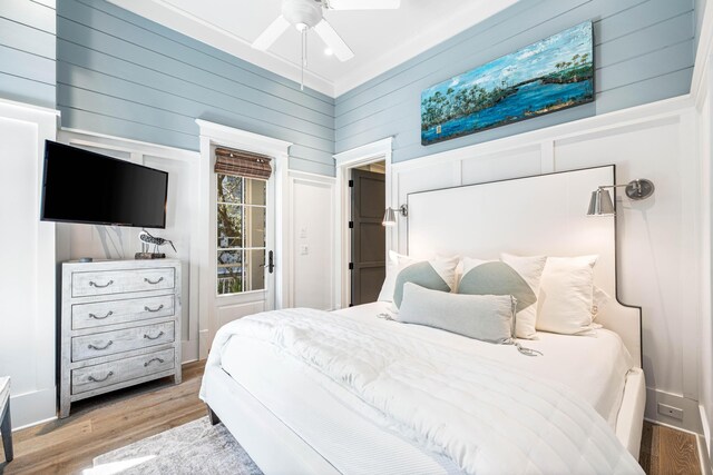 bedroom featuring ornamental molding, light hardwood / wood-style flooring, wood walls, and ceiling fan