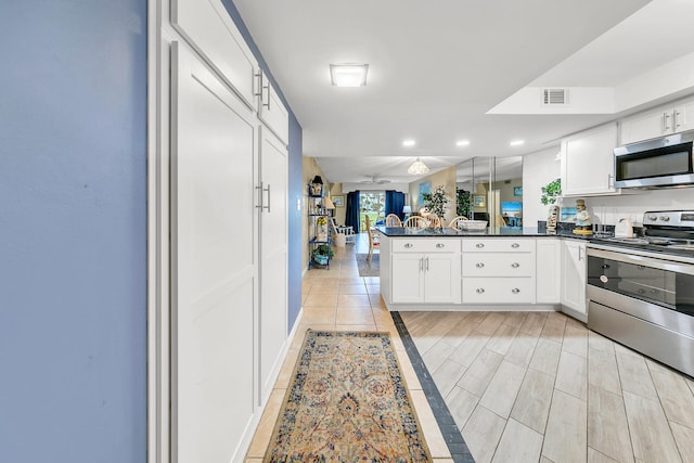 kitchen featuring white cabinets, stainless steel appliances, kitchen peninsula, and light hardwood / wood-style flooring