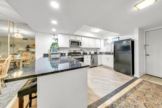 kitchen with a kitchen bar, stainless steel appliances, kitchen peninsula, and white cabinets