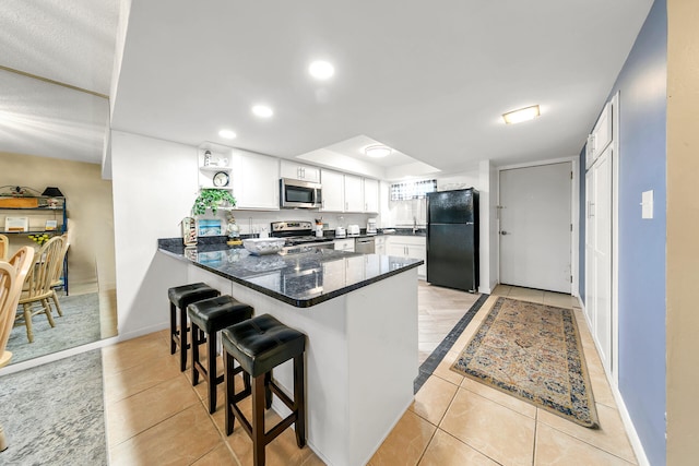 kitchen featuring light tile patterned floors, kitchen peninsula, a breakfast bar, appliances with stainless steel finishes, and white cabinets