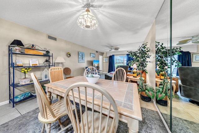 dining room featuring ceiling fan with notable chandelier, a textured ceiling, and light tile patterned floors