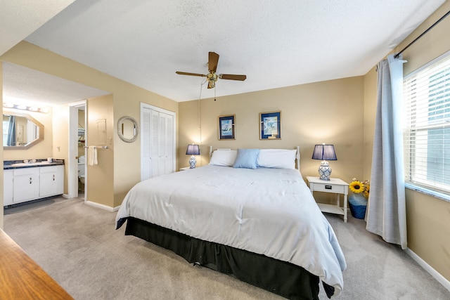 carpeted bedroom with a textured ceiling, ensuite bathroom, and ceiling fan