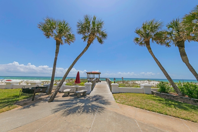 view of community featuring a water view, a lawn, and a beach view