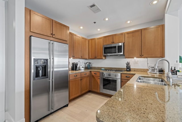 kitchen with visible vents, light wood-type flooring, a sink, light stone counters, and appliances with stainless steel finishes