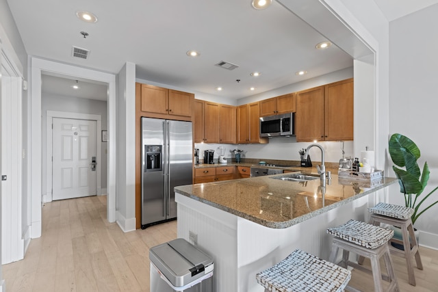 kitchen featuring light hardwood / wood-style flooring, appliances with stainless steel finishes, sink, dark stone counters, and kitchen peninsula