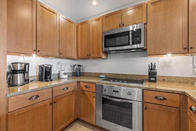 kitchen with light stone countertops, appliances with stainless steel finishes, and brown cabinets