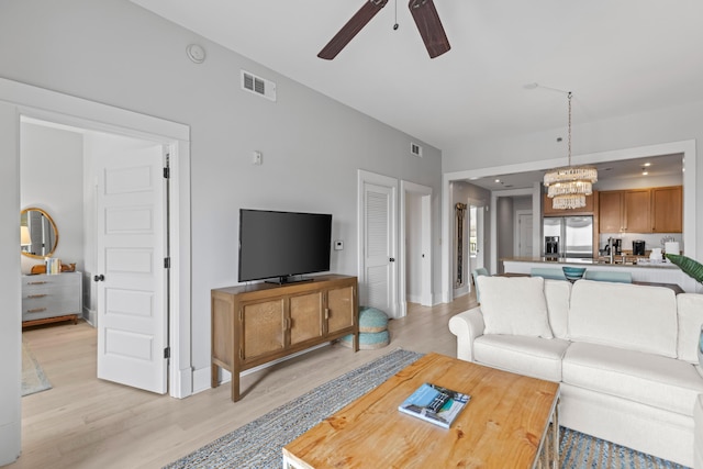 living room featuring visible vents, baseboards, light wood-style flooring, and ceiling fan with notable chandelier