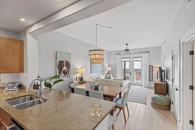 kitchen with ceiling fan with notable chandelier, decorative light fixtures, light hardwood / wood-style flooring, sink, and light stone counters