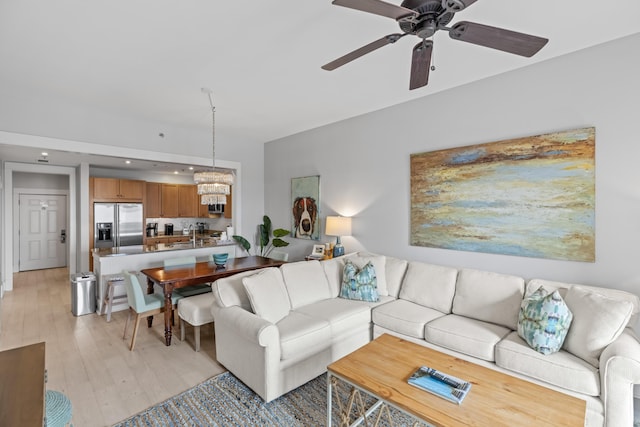 living room with ceiling fan with notable chandelier and light wood-type flooring