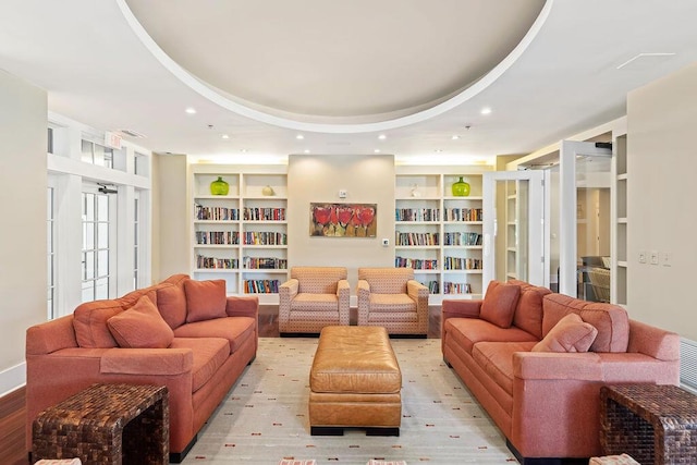 living room with recessed lighting, built in shelves, a raised ceiling, and light wood-style floors