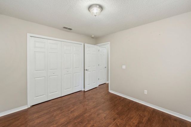 unfurnished bedroom featuring dark wood-type flooring, a closet, and a textured ceiling