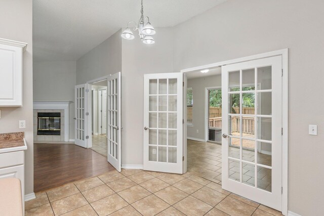 unfurnished dining area with a tile fireplace, french doors, light hardwood / wood-style floors, a notable chandelier, and lofted ceiling