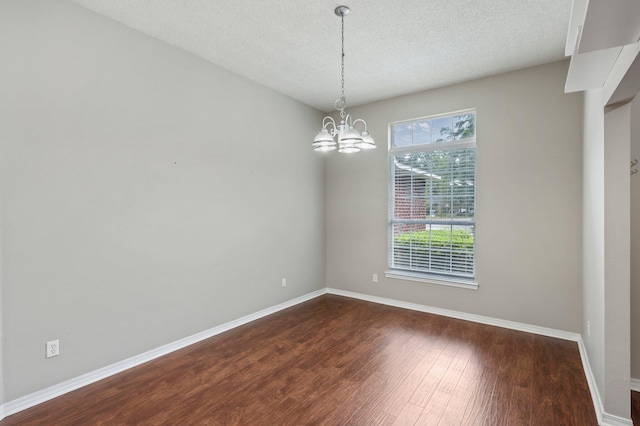 spare room featuring a textured ceiling, an inviting chandelier, and dark hardwood / wood-style flooring