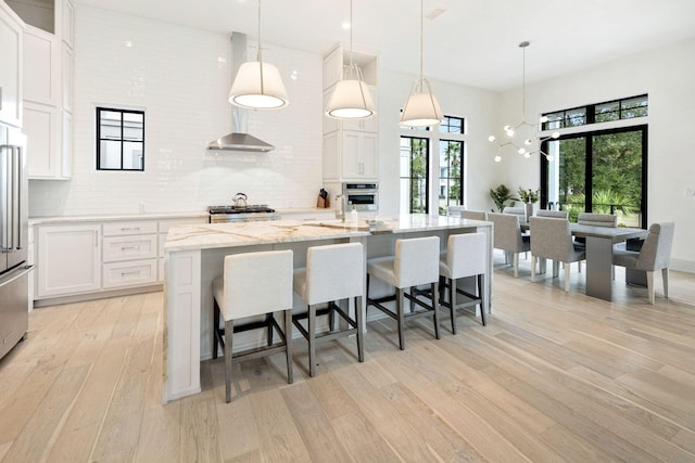 kitchen with a large island, light hardwood / wood-style flooring, decorative light fixtures, white cabinetry, and stainless steel appliances