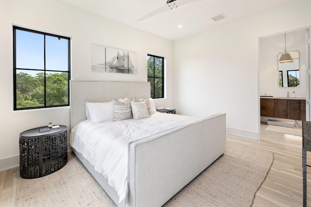 bedroom with ensuite bathroom, multiple windows, ceiling fan, and light hardwood / wood-style floors