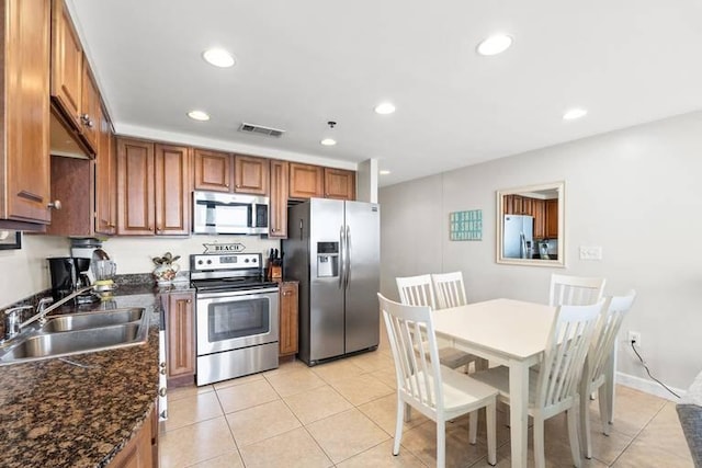 kitchen featuring stainless steel appliances, dark stone countertops, light tile patterned floors, and sink