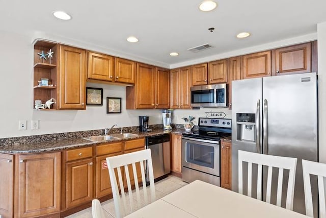 kitchen featuring appliances with stainless steel finishes, dark stone countertops, sink, and light tile patterned floors