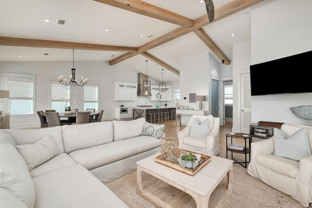 living room with a chandelier, light hardwood / wood-style floors, and lofted ceiling with beams