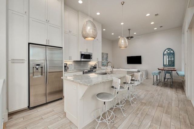 kitchen featuring wood finish floors, open floor plan, an island with sink, stainless steel appliances, and a sink