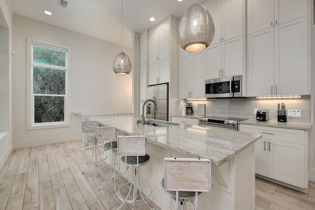 kitchen featuring light hardwood / wood-style flooring, stainless steel appliances, sink, an island with sink, and pendant lighting