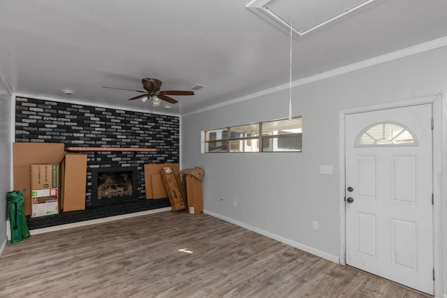 foyer entrance with ceiling fan, ornamental molding, wood-type flooring, brick wall, and a fireplace