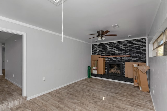 unfurnished living room featuring wood-type flooring, ornamental molding, a brick fireplace, and ceiling fan