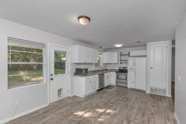 kitchen with pendant lighting, sink, white cabinetry, stainless steel appliances, and light wood-type flooring