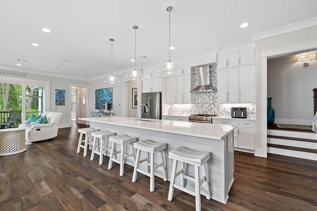 kitchen with wall chimney range hood, white cabinetry, hanging light fixtures, high quality appliances, and a large island with sink