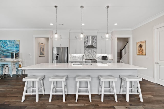 kitchen with wall chimney range hood, sink, appliances with stainless steel finishes, white cabinets, and a large island with sink