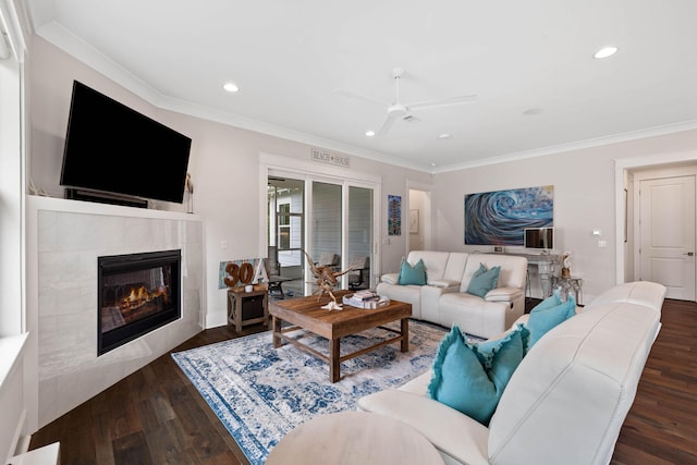 living room with dark wood-type flooring, ceiling fan, crown molding, and a tile fireplace