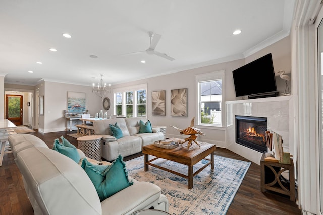 living room featuring crown molding, dark hardwood / wood-style floors, a tiled fireplace, and ceiling fan with notable chandelier