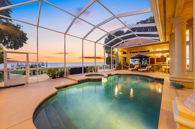 pool at dusk featuring glass enclosure, an in ground hot tub, a water view, and a patio