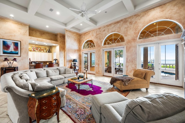 tiled living room with beam ceiling, coffered ceiling, a towering ceiling, ceiling fan, and french doors