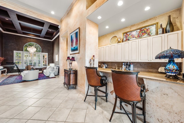 kitchen featuring a breakfast bar, beam ceiling, coffered ceiling, a towering ceiling, and light tile patterned floors