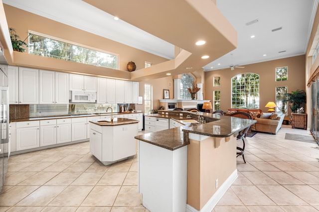 kitchen with ornamental molding, ceiling fan, light tile patterned flooring, and a kitchen island with sink