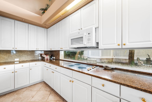 kitchen featuring dark stone counters, tasteful backsplash, white cabinets, white appliances, and light tile patterned floors