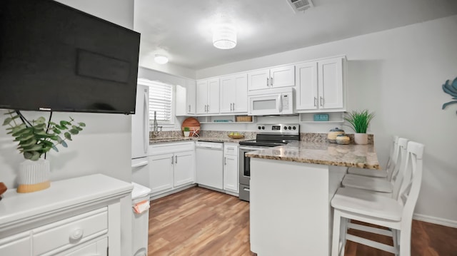 kitchen featuring white cabinets, white appliances, kitchen peninsula, and a breakfast bar area